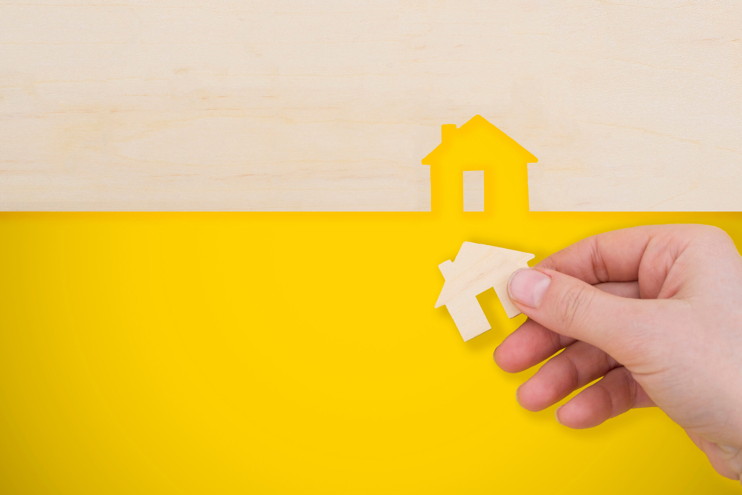 hand places a model house on yellow background.
